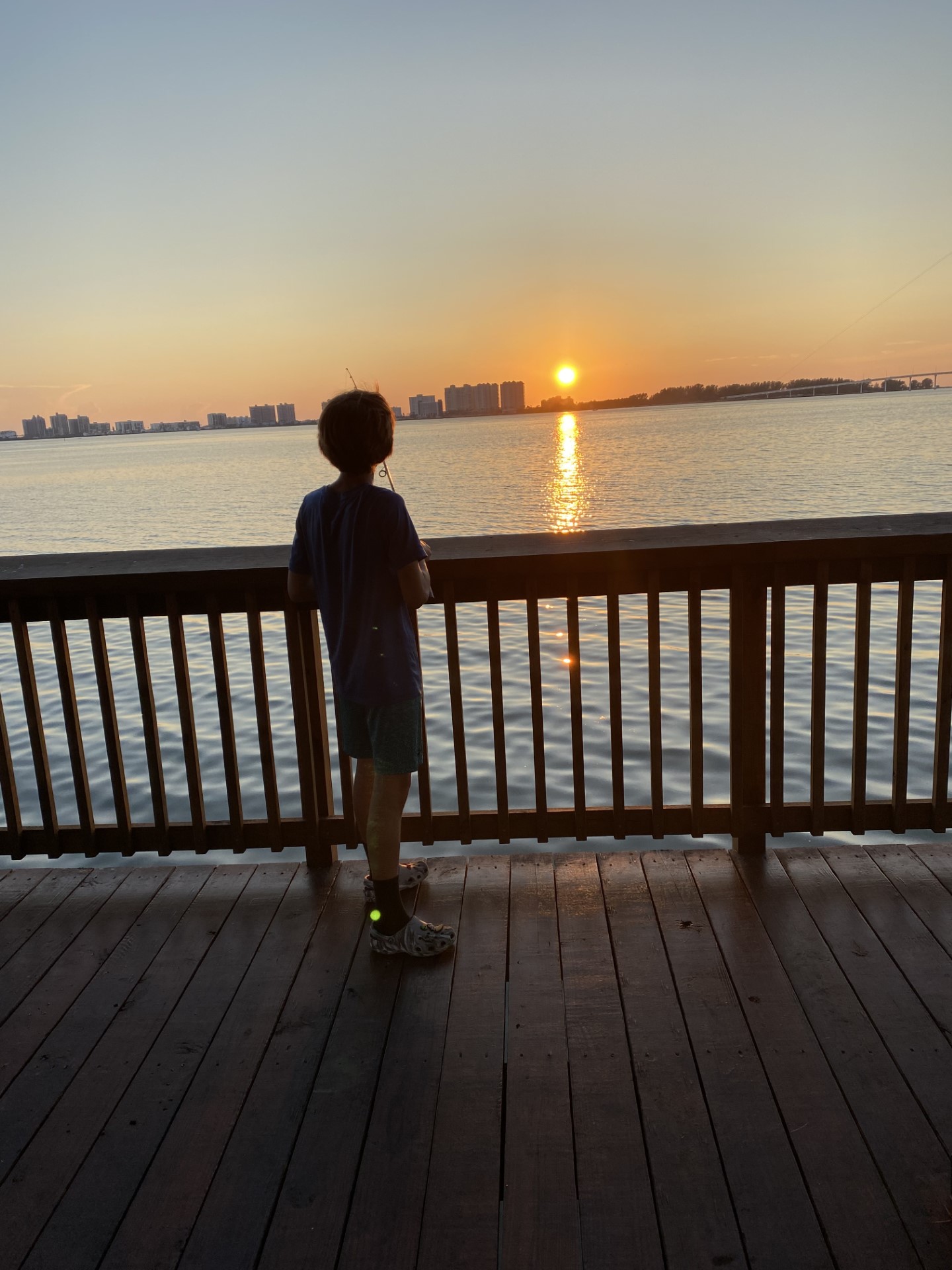 Young angler fishing from a pier at sunset